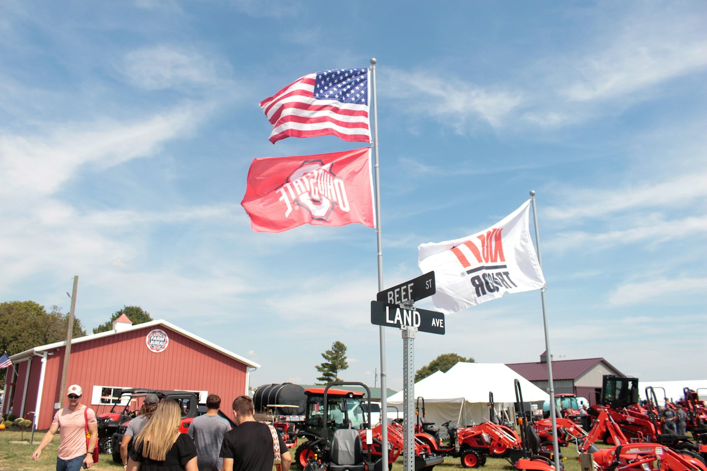 People walk past tractors displayed at an outdoor agricultural event.