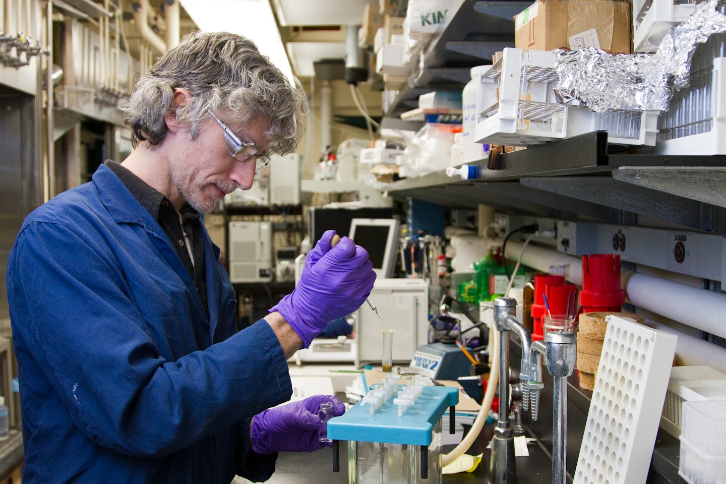 Man in lab coat pipetting liquid into a test tube.